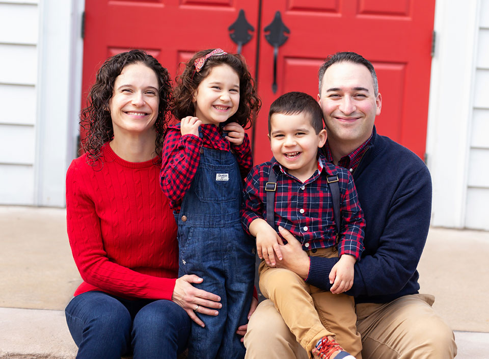 family of four posing in front of red door for family photos