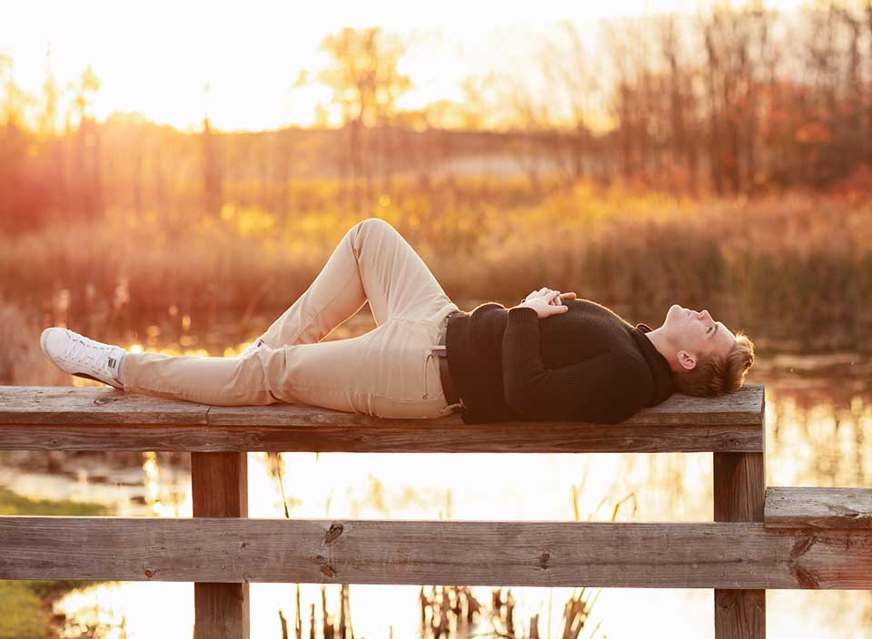 senior boy lying on dock in golden hour light by photographer Corie Walker