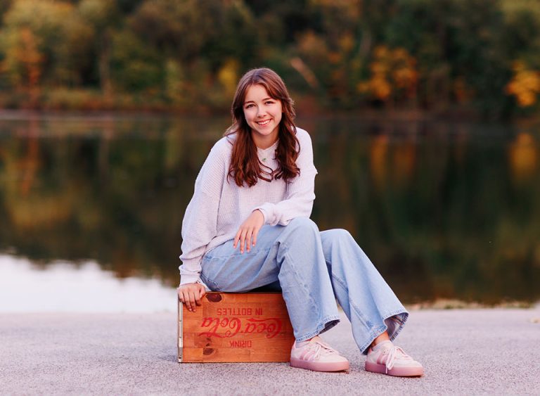 senior girl sitting on box in front of lake