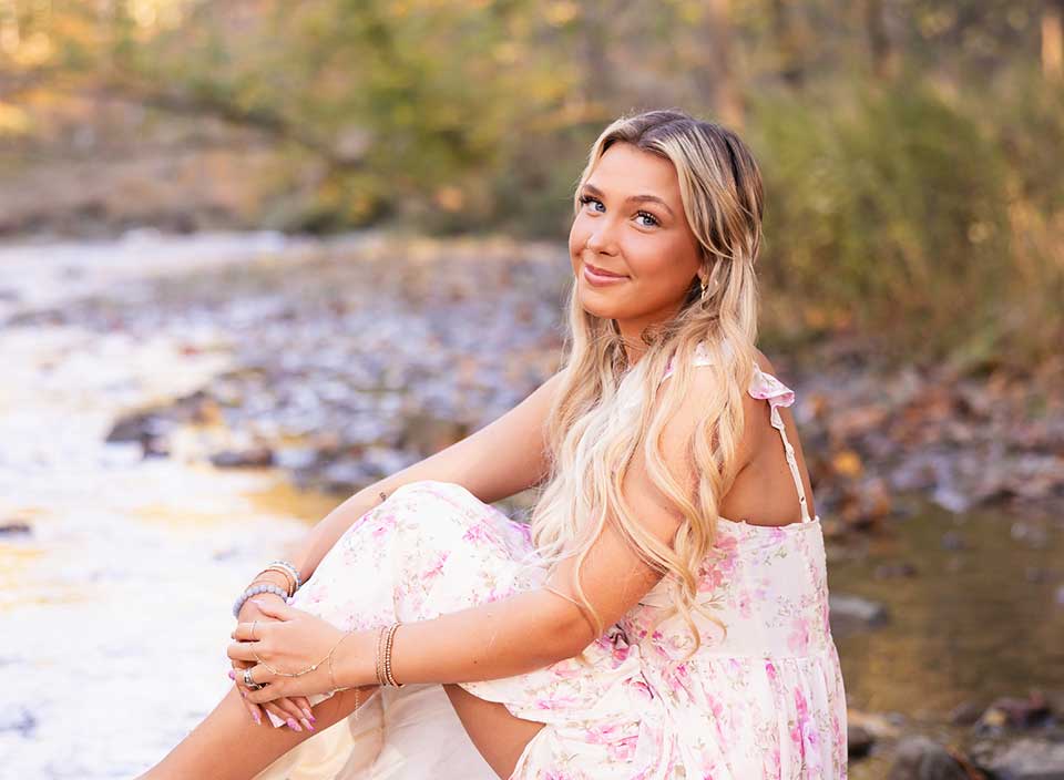 senior girl in dress sitting on riverbank