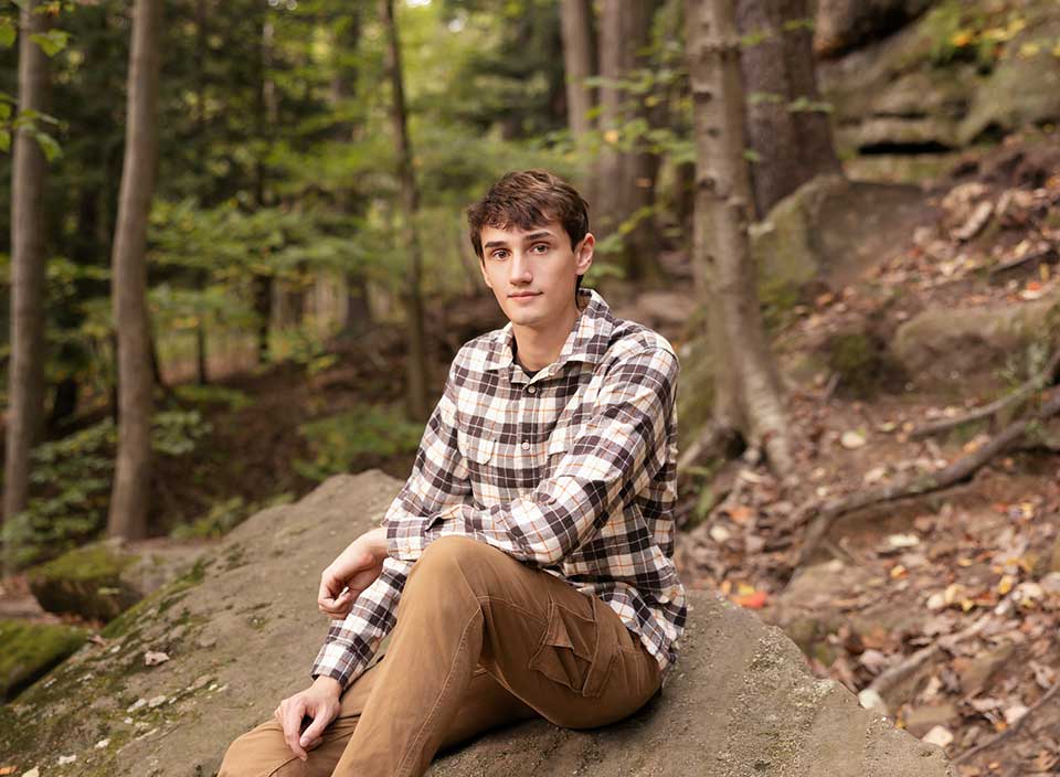 boy sitting on rock in woods for senior pictures with Corie Walker Photography