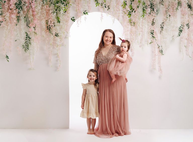 mom and two little girls posing in front of floral arch