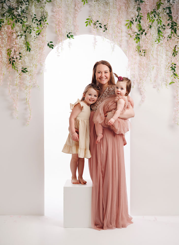 mom and two little girls posing in front of floral arch