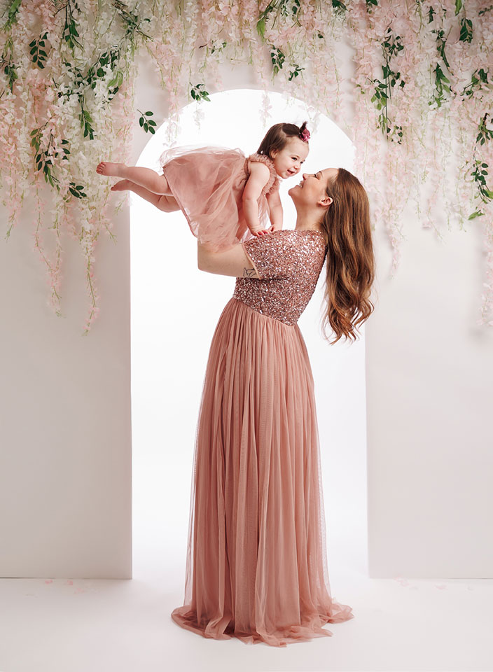 mom and baby girl posing in front of floral arch