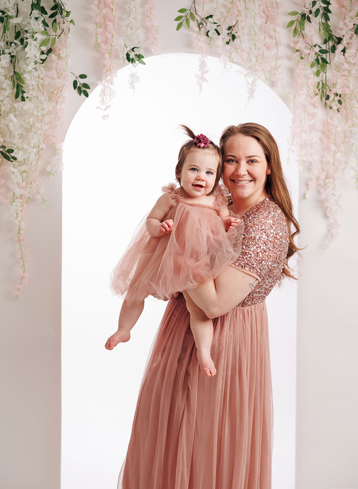 mom and baby girl posing in front of floral arch