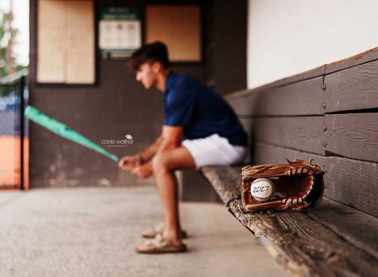 high school boy posing for senior pictures in baseball dugout