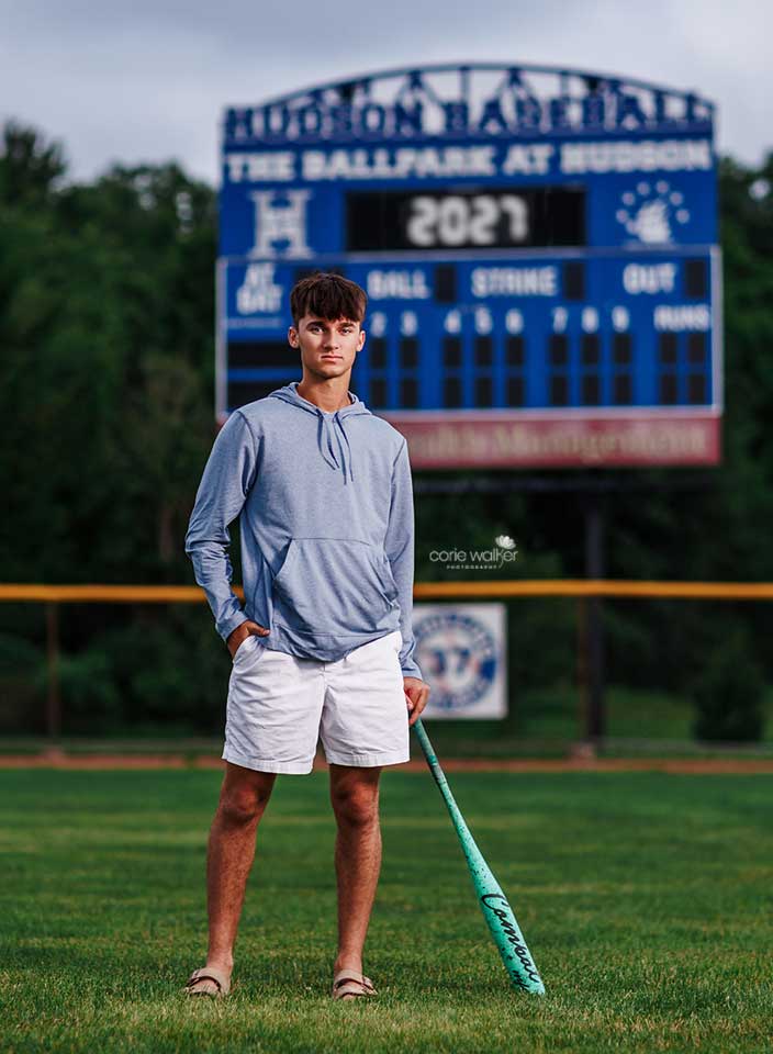 high school boy posing for senior pictures on baseball field