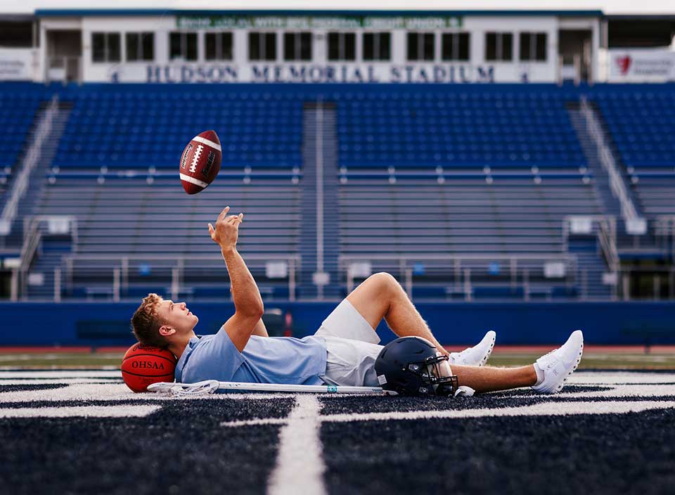 high school boy lying on football field with gear for senior pictures