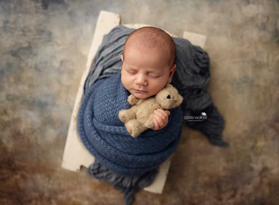 newborn baby hugging small bear stuffie