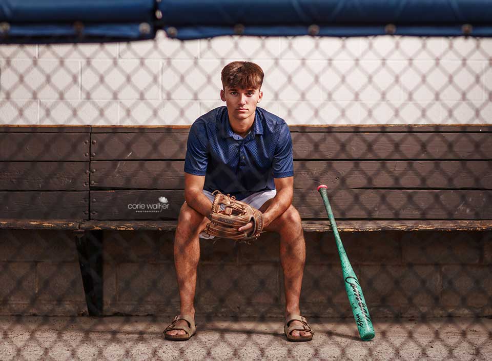 high school boy posing for senior pictures in baseball dugout