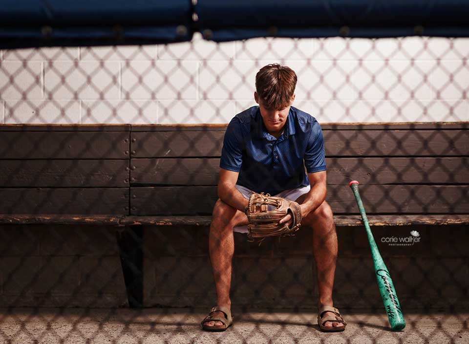 high school boy posing for senior pictures in baseball dugout