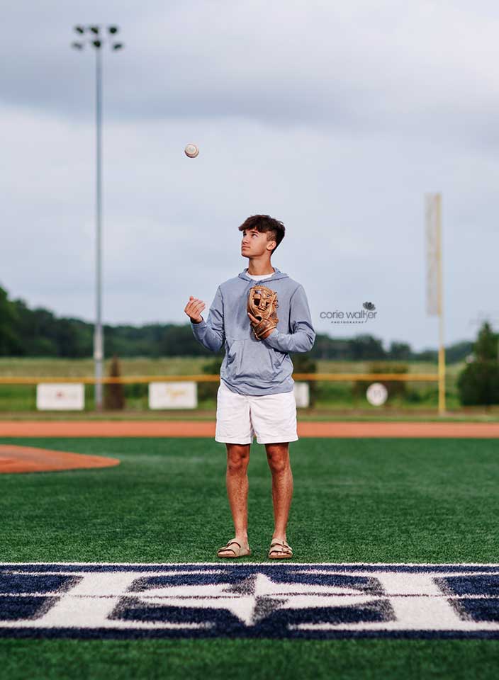 high school boy tossing baseball for senior pictures in baseball field