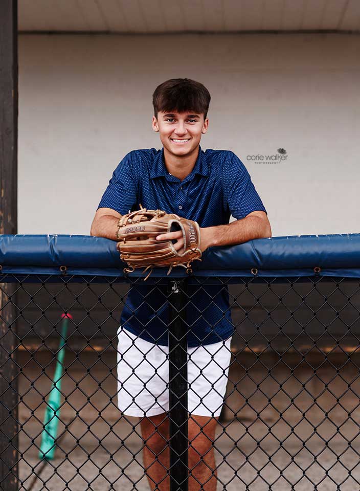 high school boy posing for senior pictures in baseball dugout