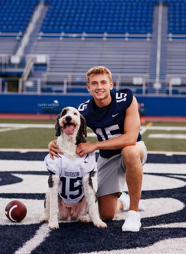 senior boy posing with his dog for photo on football field