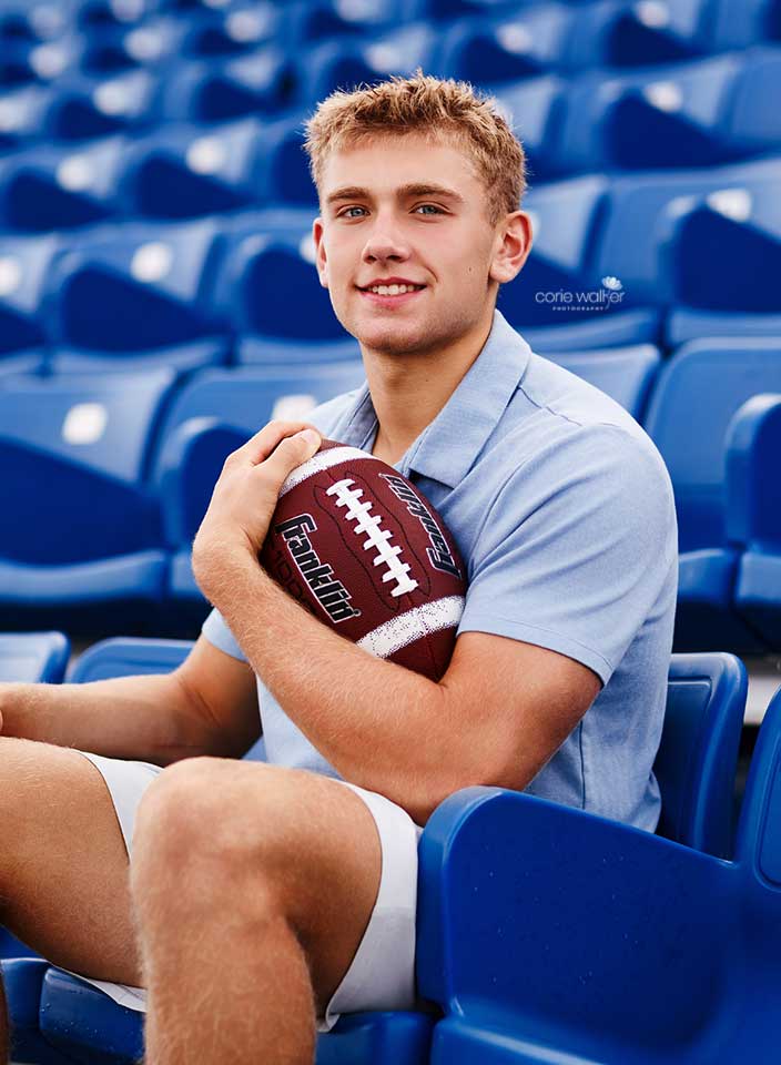 senior boy posing for photo with football