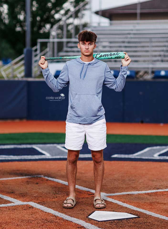high school boy posing for senior pictures on baseball field