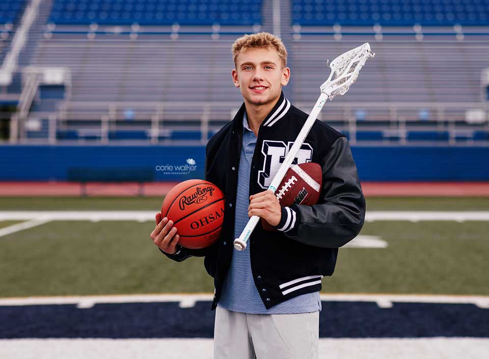 high school athlete posing for senior photos with football, basketball and lax stick